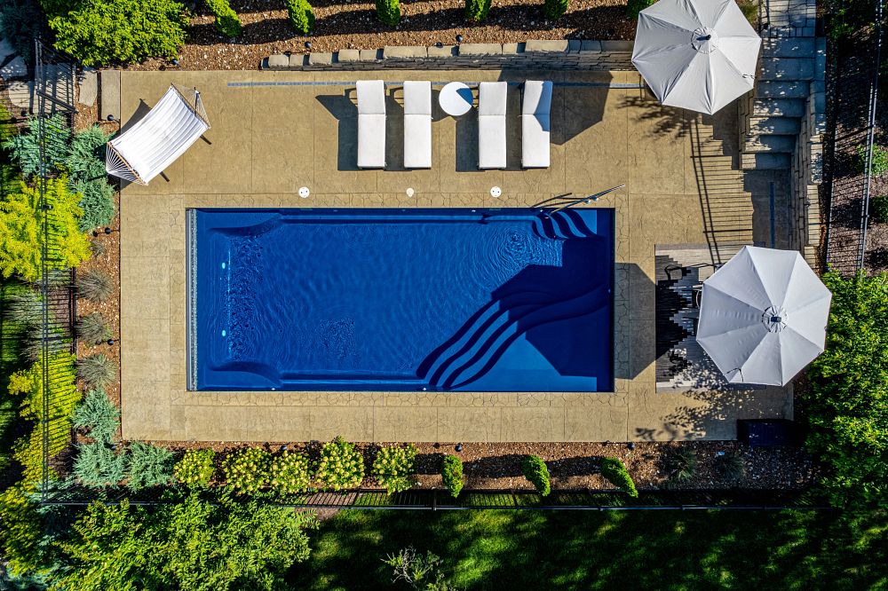 rectangular fiberglass pool surrounded by lounge chairs and umbrellas in southern backyard