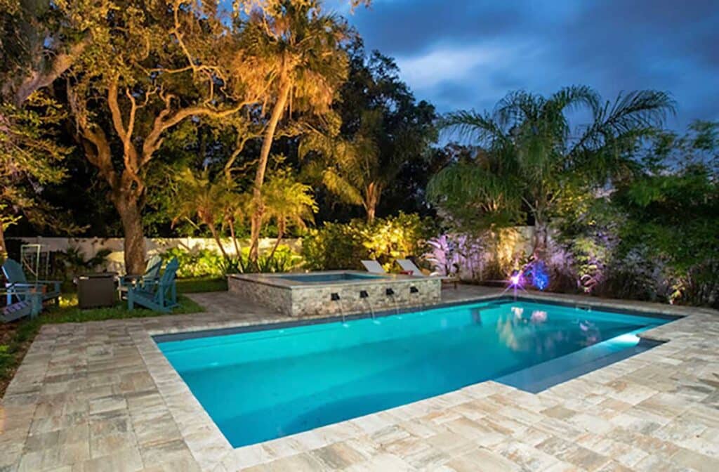 Fiberglass pool illuminated at night with soft lighting and tropical landscaping in a Fort Lauderdale backyard