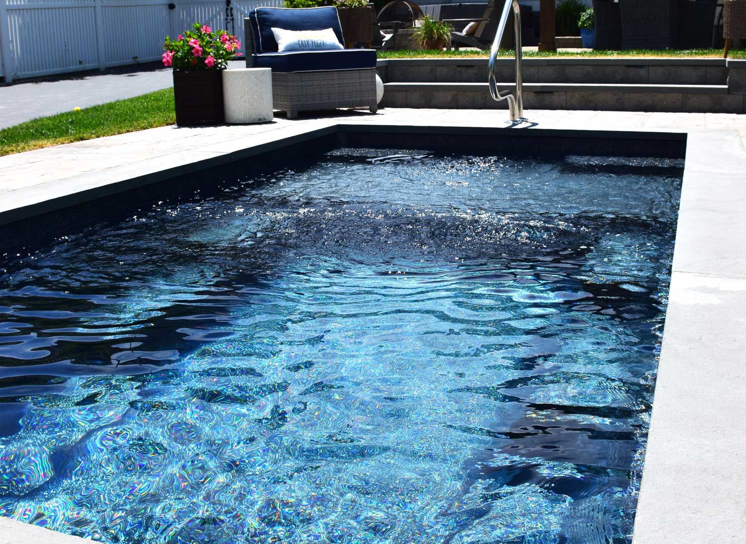 Small plunge pool with sparkling water and sunlit patio, accented by potted plants and a privacy fence.