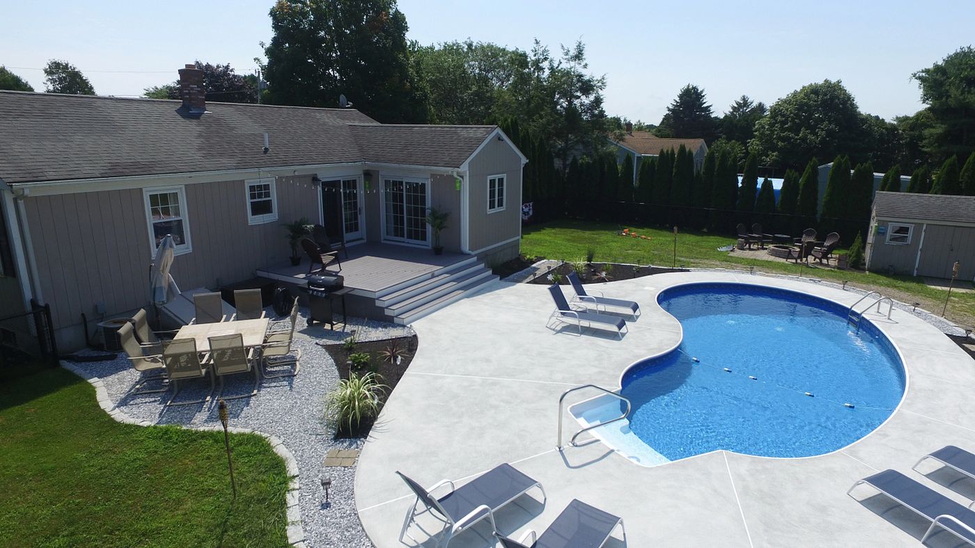 Aerial view of a freeform Crescent vinyl liner pool featuring a light blue liner and surrounded by wide white concrete decking.