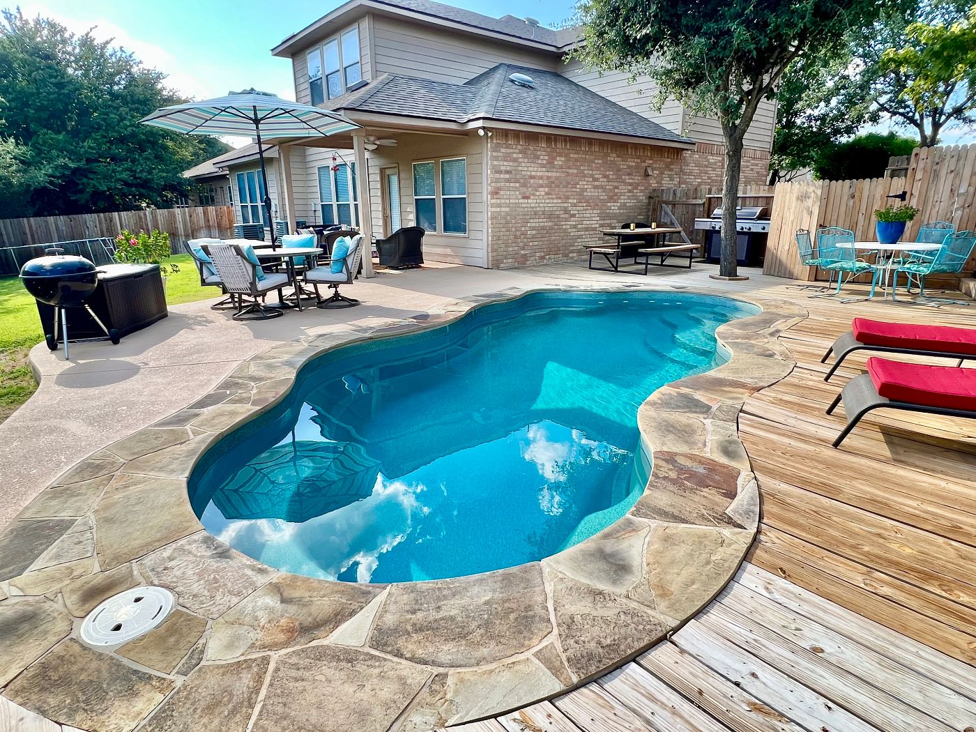 Freeform Bermuda Latham fiberglass pool surrounded by natural stone coping and a paver patio.