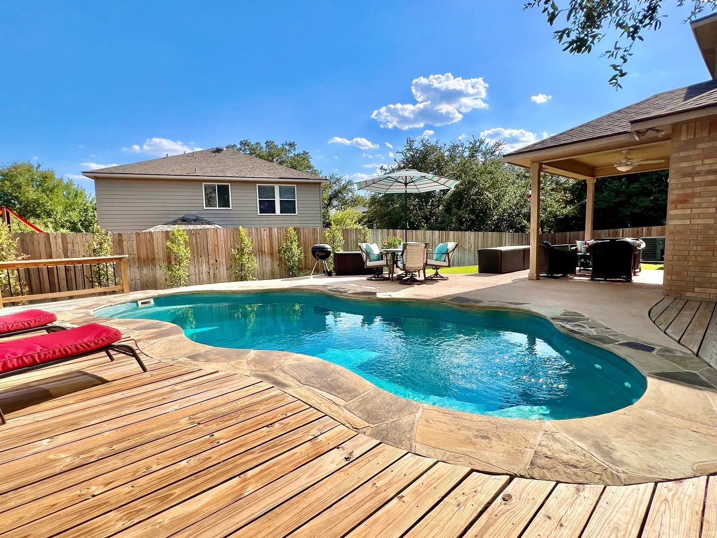 Fiberglass pool beside a wooden deck and covered patio.