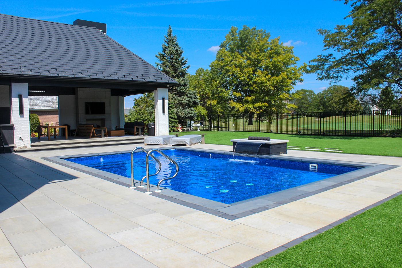 Rectangular vinyl liner pool with gray coping, modern tile work, and an elegant deck water feature.