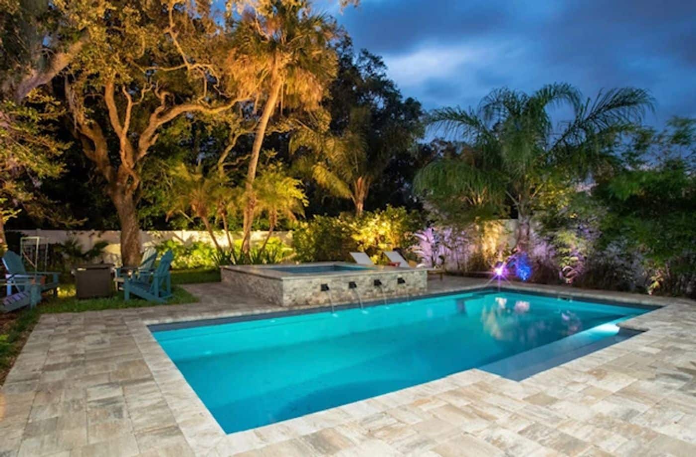 Rectangular fiberglass pool and elevated spa beautifully illuminated by underwater lighting in a tropical backyard.