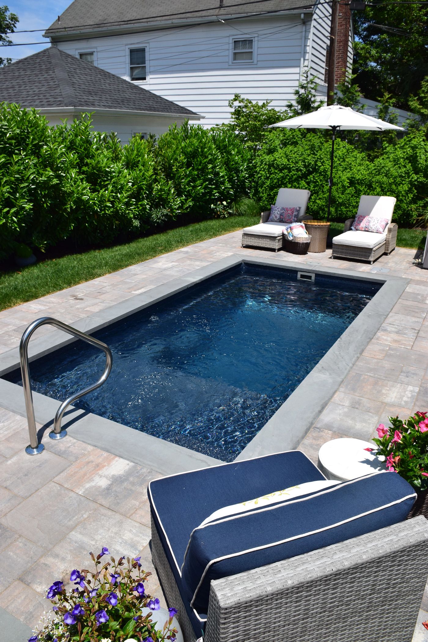 Rectangular fiberglass plunge pool with dark interior, light paver surround, and stainless steel access handrail.